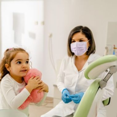 Young child holding a stuffed toy during a first dental visit with a pediatric dentist.