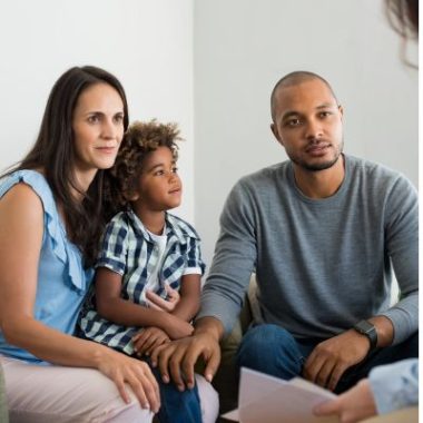 Parents sit with their child while talking to a professional.